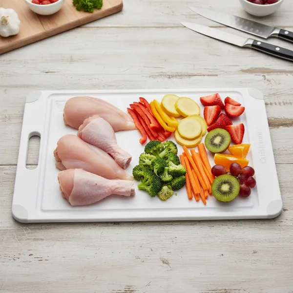 Various foods being prepared on a Cuisinart non-slip plastic board: meat, vegetables, and fruit